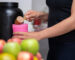 Healthy women preparing a whey protein after doing weight training in the kitchen with fresh fruits as a blurred foreground.
